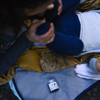 Mum changing baby outdoors on change mat with jar of nappy cream on display
