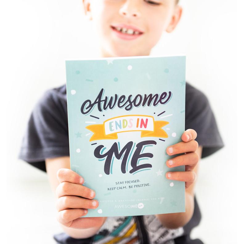 A child holding a gratitude journal with a blue cover and the text 'Awesome ME' on it.