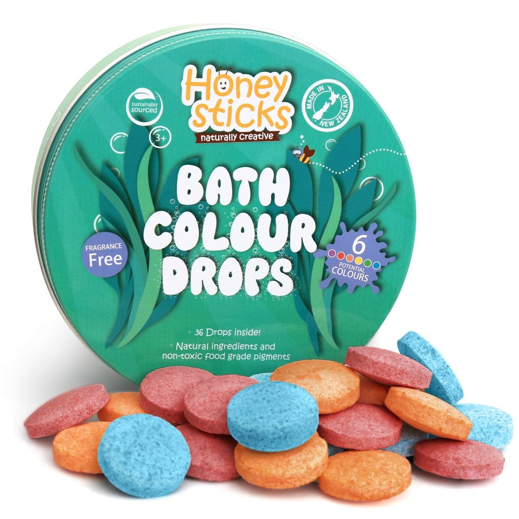 A package of Honeysticks Bath Colour Drops with multiple colorful bath fizzers displayed in front. The packaging is predominantly green with images of plants and text describing the product as natural and non-toxic.