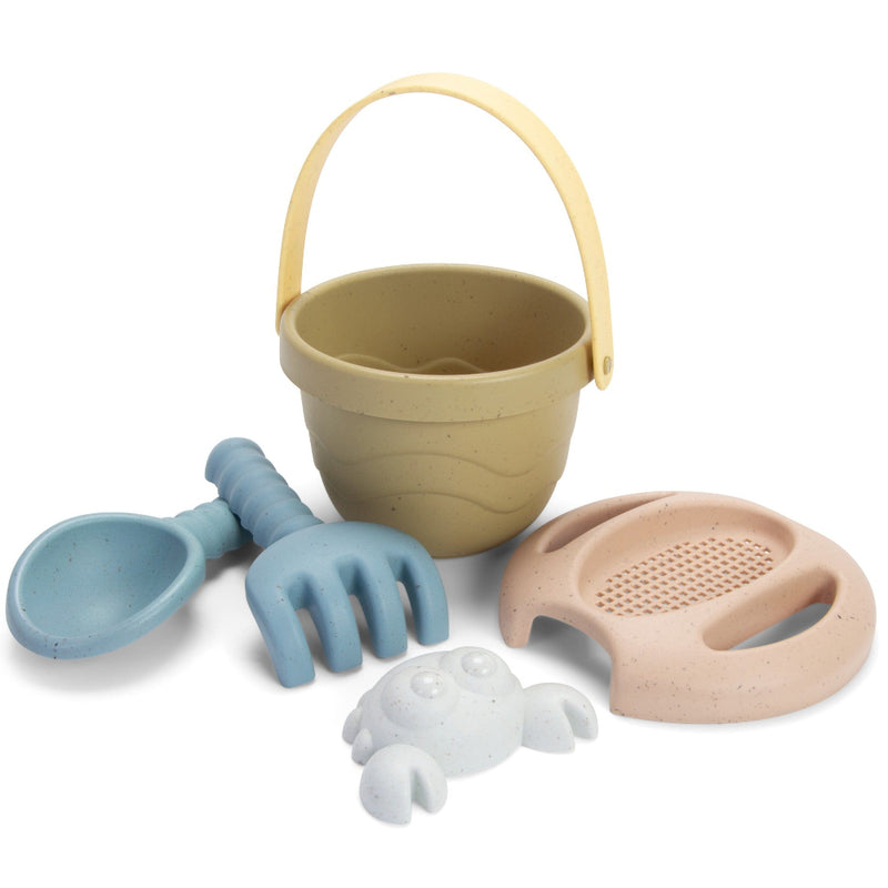 A set of small bioplastic beach toys including a bucket, scoop, rake, sieve, and sand mould, primarily in beige and blue colors.