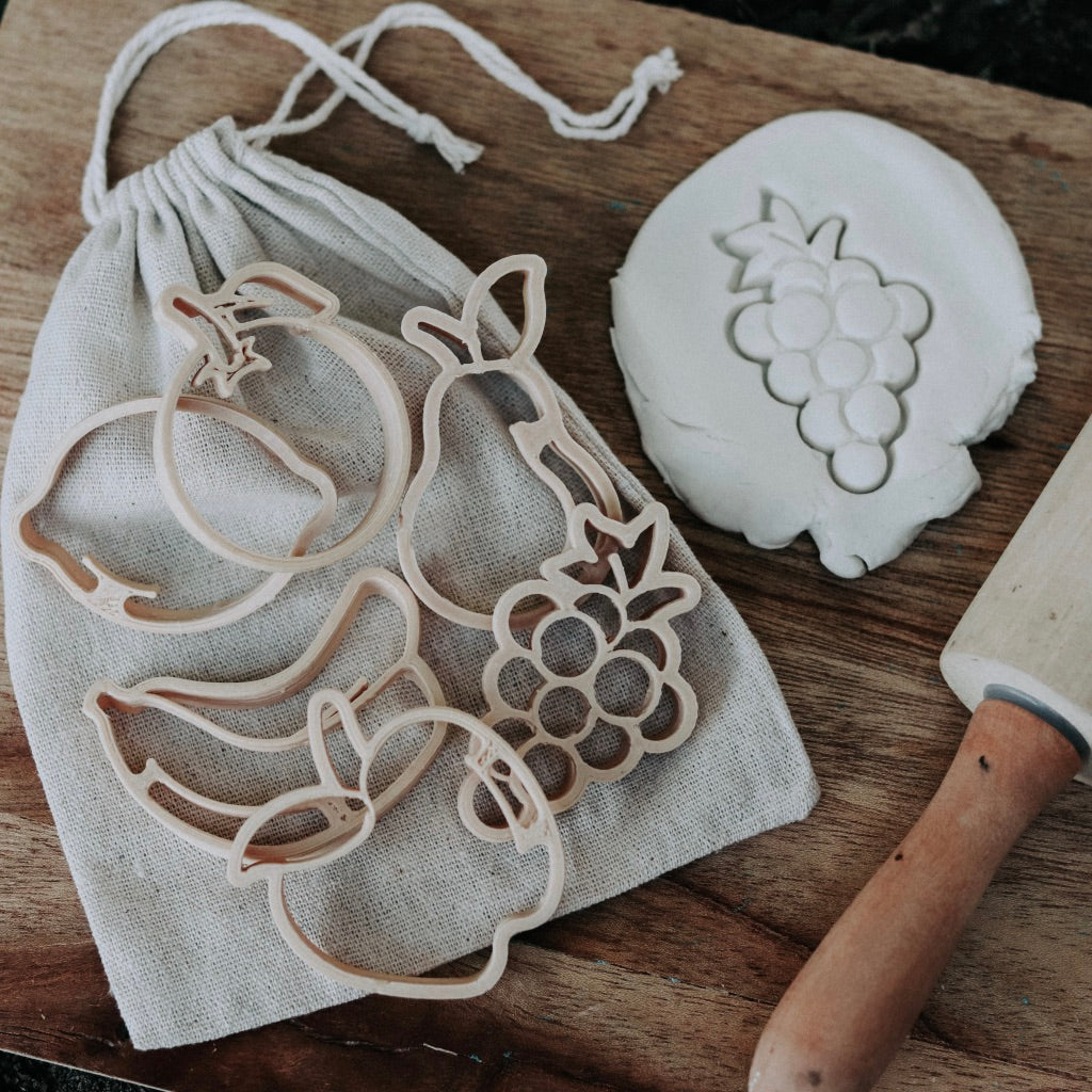 Fruit shaped eco dough cutters resting on a cotton bag on a wooden chopping board