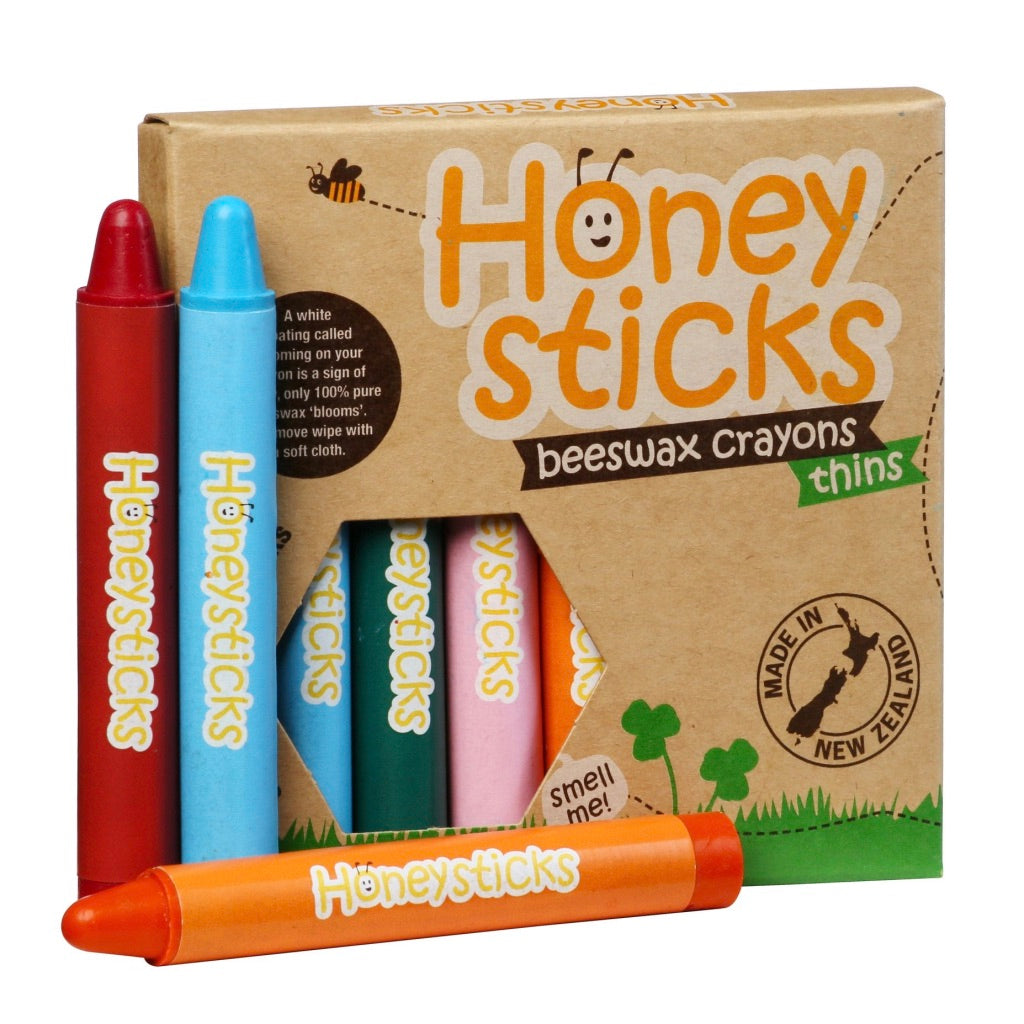 A pack of Honeysticks Beeswax Crayons Thins with multiple colors displayed in front of the packaging. The packaging is labeled 'HONEY STICKS' and has images of bees and a kiwi fruit, indicating that the product is made in New Zealand.