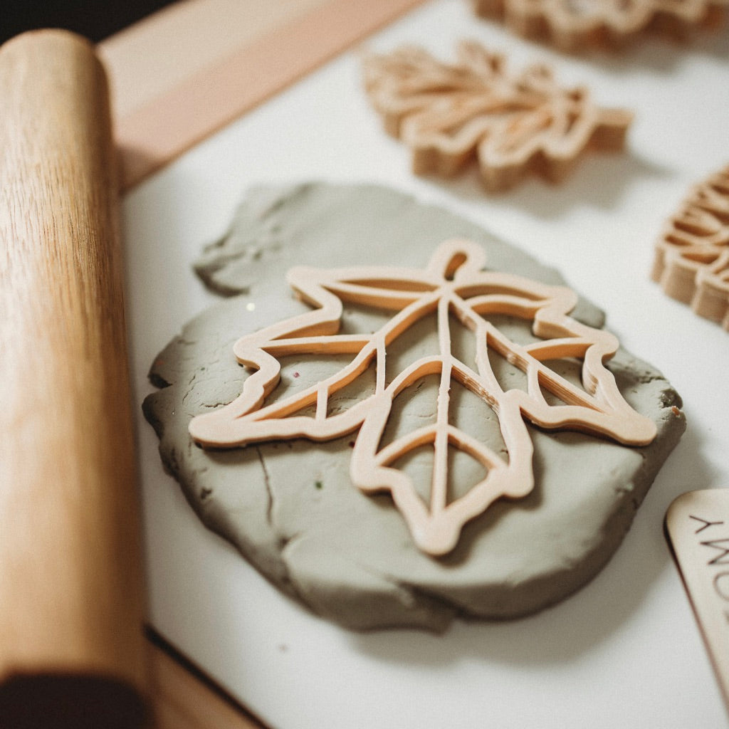 Leaf shaped dough cutters pressed into clay on a white surface