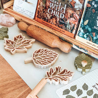 Leaf dough cutters with wooden rolling pin and books sitting on wooden table
