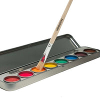 A set of Honeysticks natural watercolour paints with a paintbrush, including eight round paint discs in vibrant colors, contained in a metal tray.