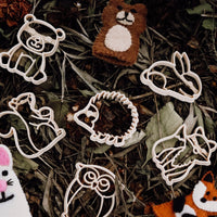 Wooden creature shaped dough cutters on dried leaves with animal finger puppets
