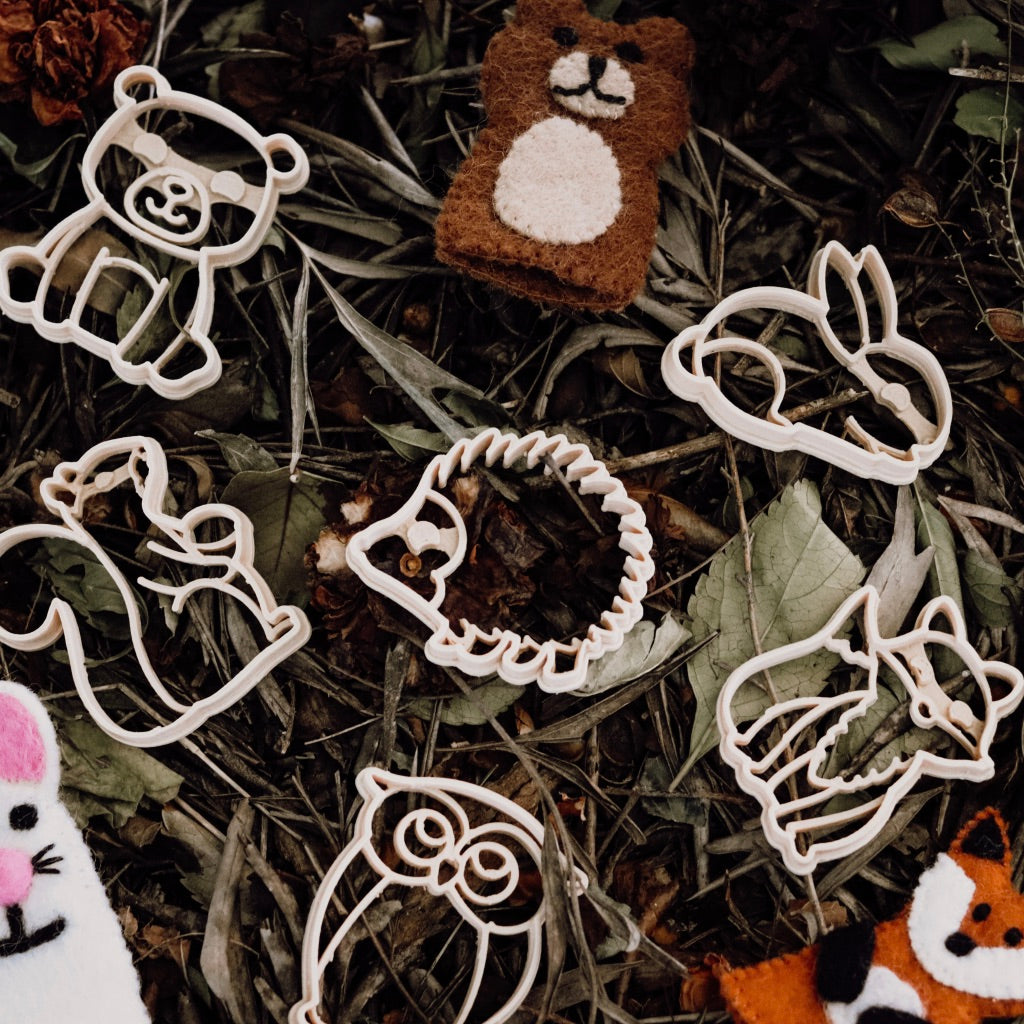 Wooden creature shaped dough cutters on dried leaves with animal finger puppets